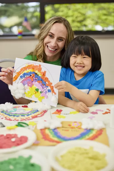 Y Staff and child proudly showcasing a rainbow art project